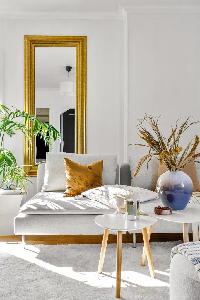 Salon lumineux au design moderne avec accents dorés Intérieur de salon lumineux avec canapé clair, miroir doré, plantes vertes et décoration soignée