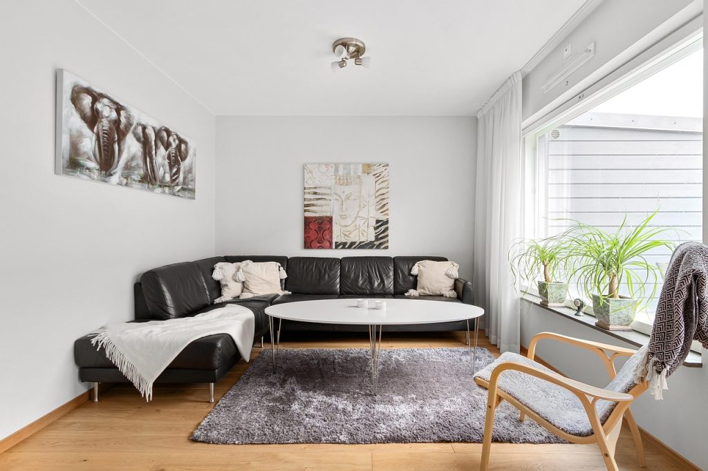Salon avec canapé d’angle, table basse ronde et lumière naturelle entrant par une fenêtre à droite