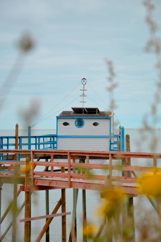 Cabane en bois bleu et blanc isolée au bord de l’eau, capturée avec une longue focale et une faible profondeur de champ